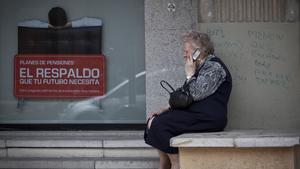 Una mujer mayor habla por teléfono móvil al lado de un cartel de planes de pensiones.