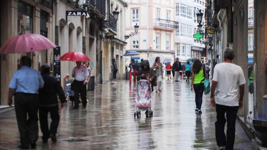 Paseantes por la calle Real de A Coruña en un día de lluvia en verano.