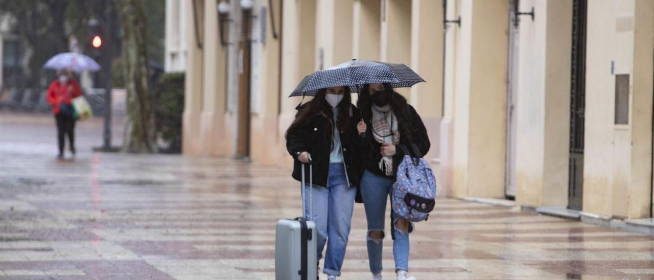 Dos chicas se protegen de la lluvia con un paraguas en Xàtiva, un día del pasado año 2021. | PERALES IBORRA