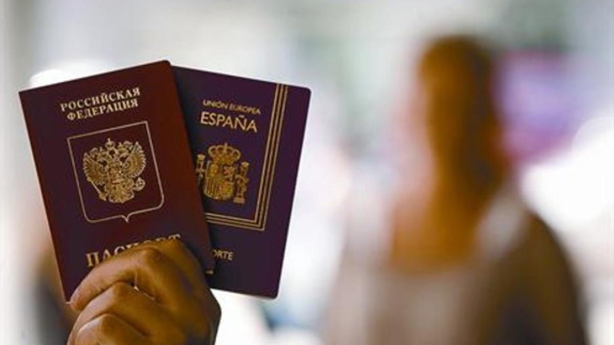 La madre, difuminada al fondo, y los dos pasaportes que ha tenido su hijo, uno ruso y uno español, el jueves.