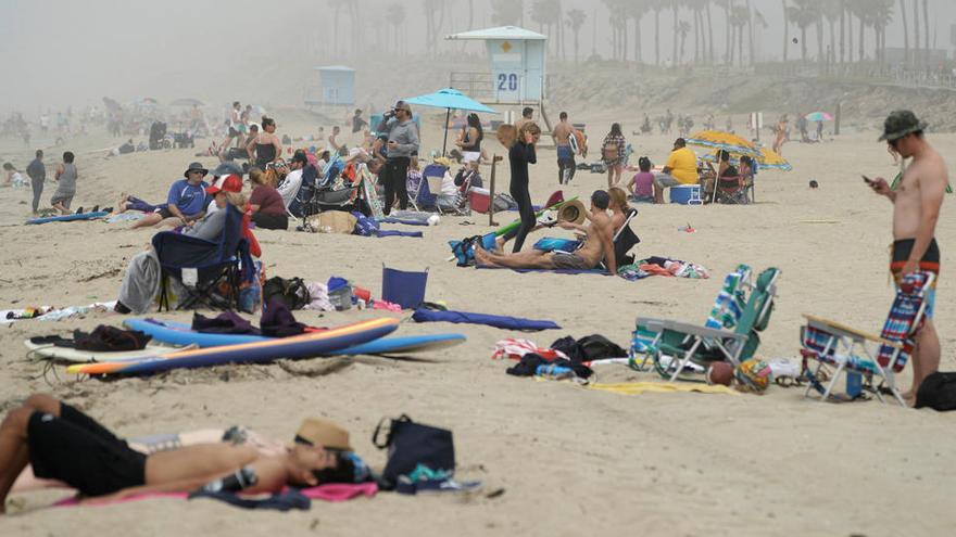 La gente se sienta en grupos en la playa de Huntington City durante el brote de la enfermedad coronavirus.