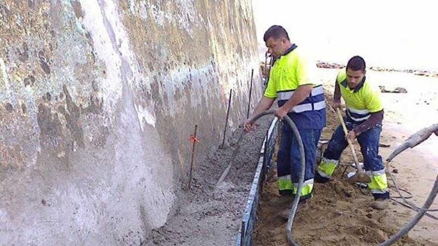 Dos operarios realizan trabajos en el muro afectado por las olas.