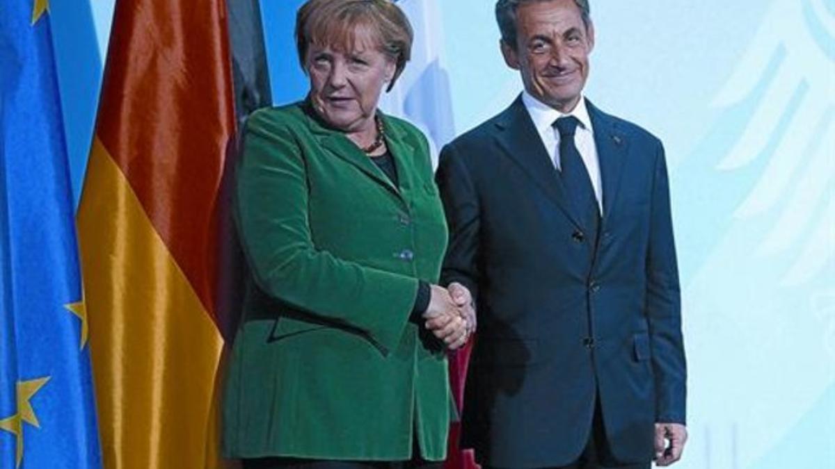 Merkel y Sarkozy se saludan, ayer, antes de atender a la prensa y tras reunirse en Berlín.