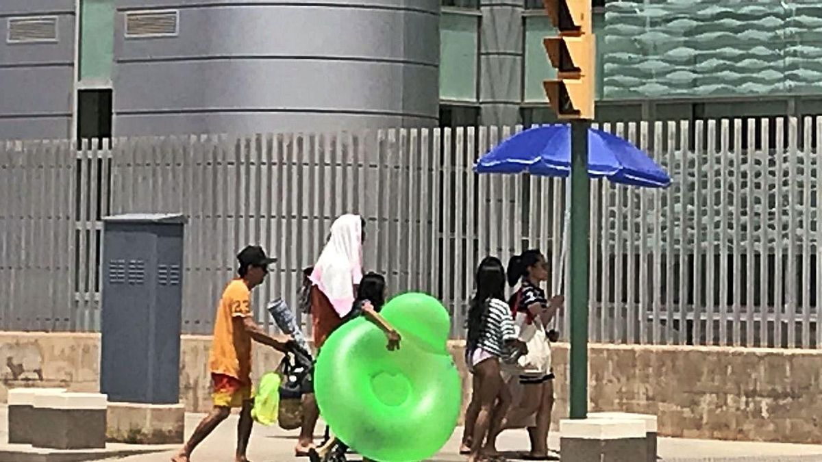 Una familia regresa de la playa con la sombrilla abierta y toallas en la cabeza. | RAÚL SANZ