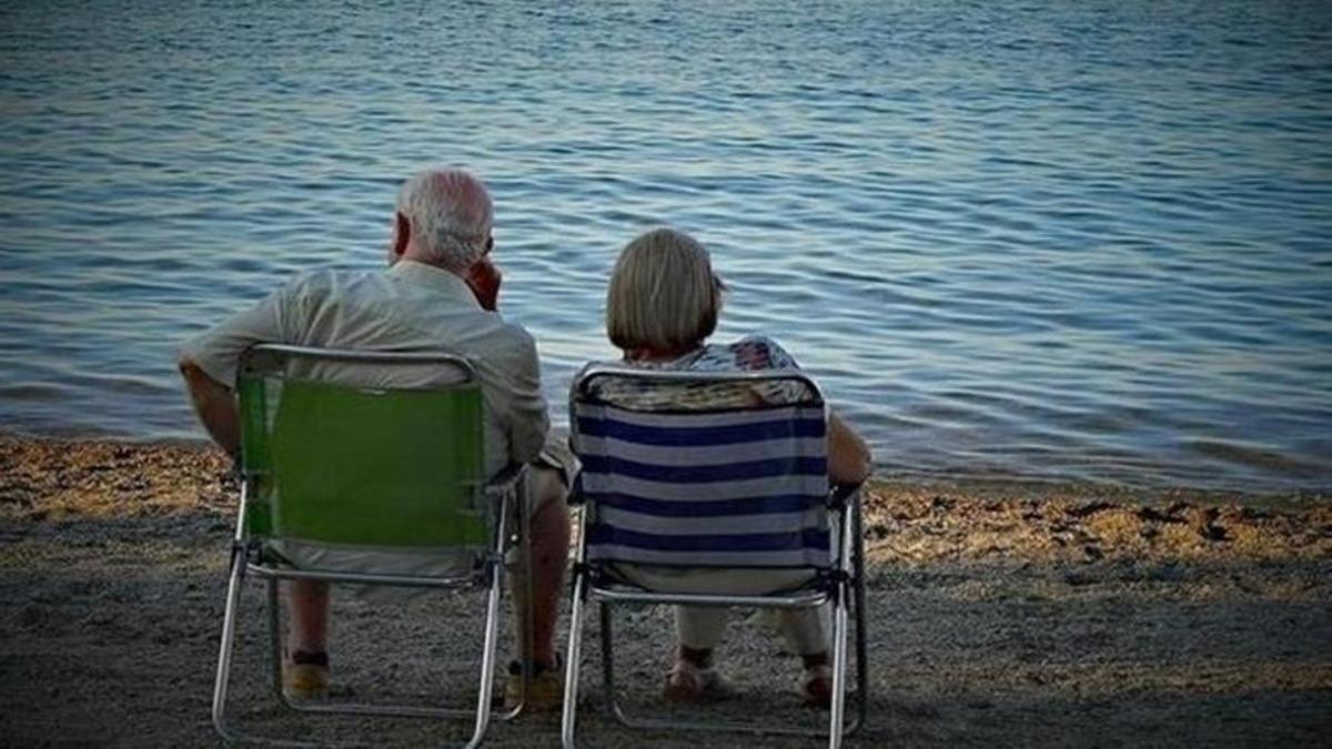 Dos pensionistas descansan sentados frente al mar