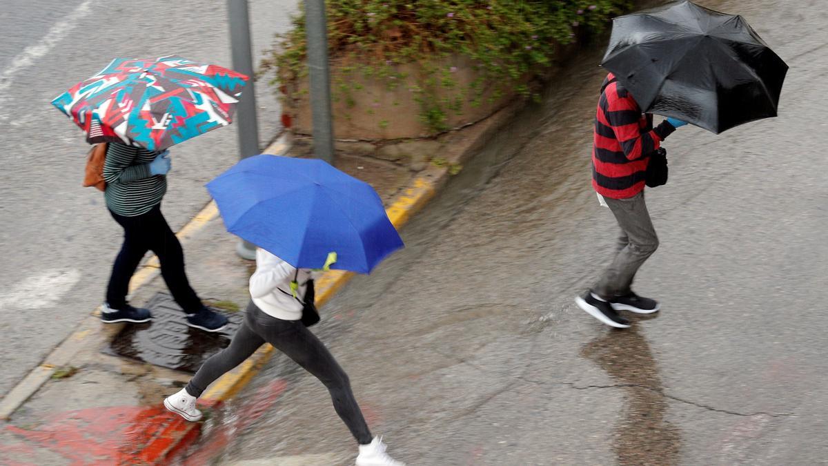 Varias personas pasean bajo la lluvia.