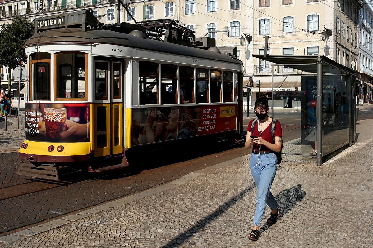 Una mujer con mascarilla camina frente a un tranvía en el centro de Lisboa