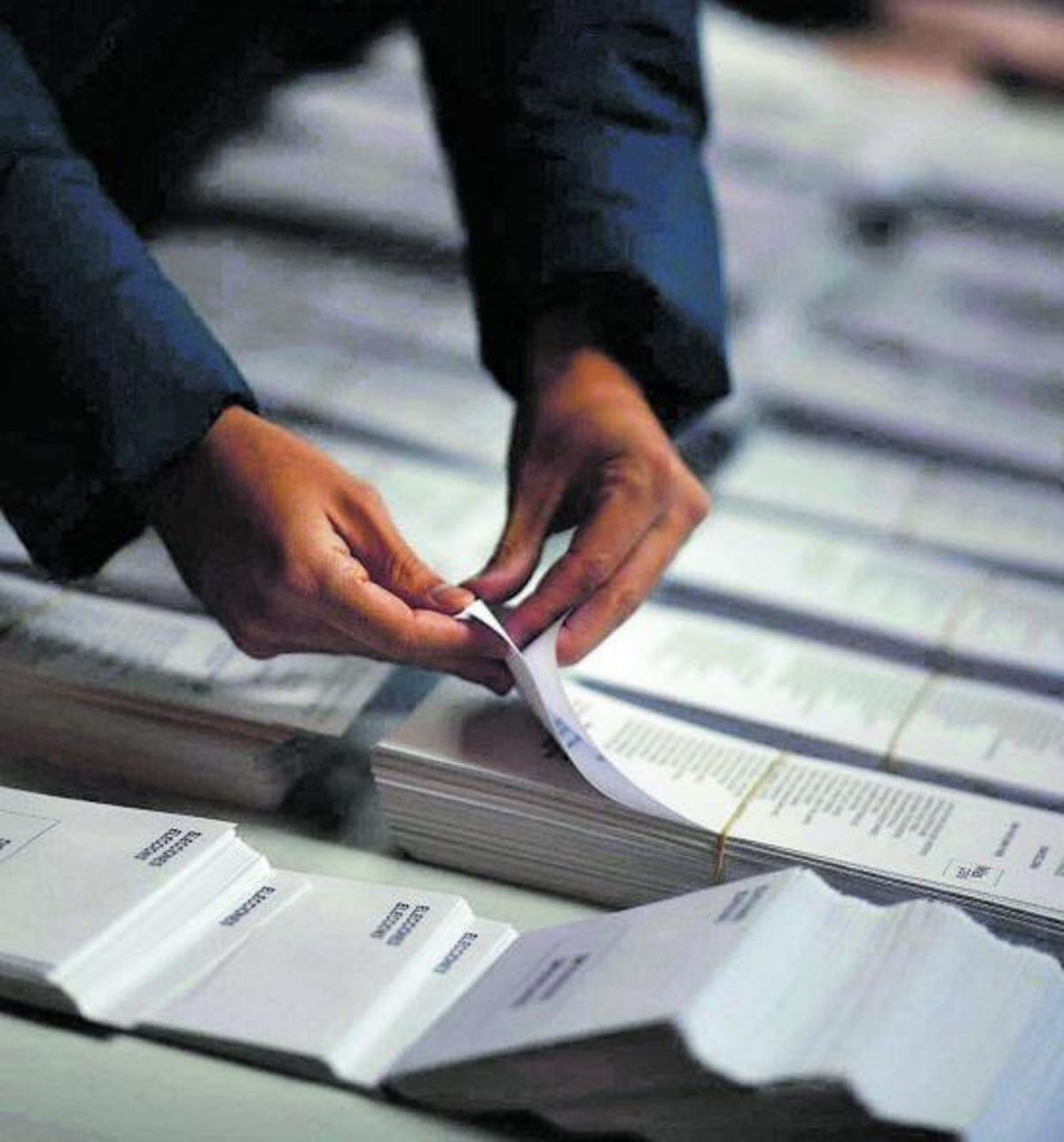Un hombre elige voto entre las papeletas dispuestas con candidaturas en unos comicios.   | // JORDI COTRINA