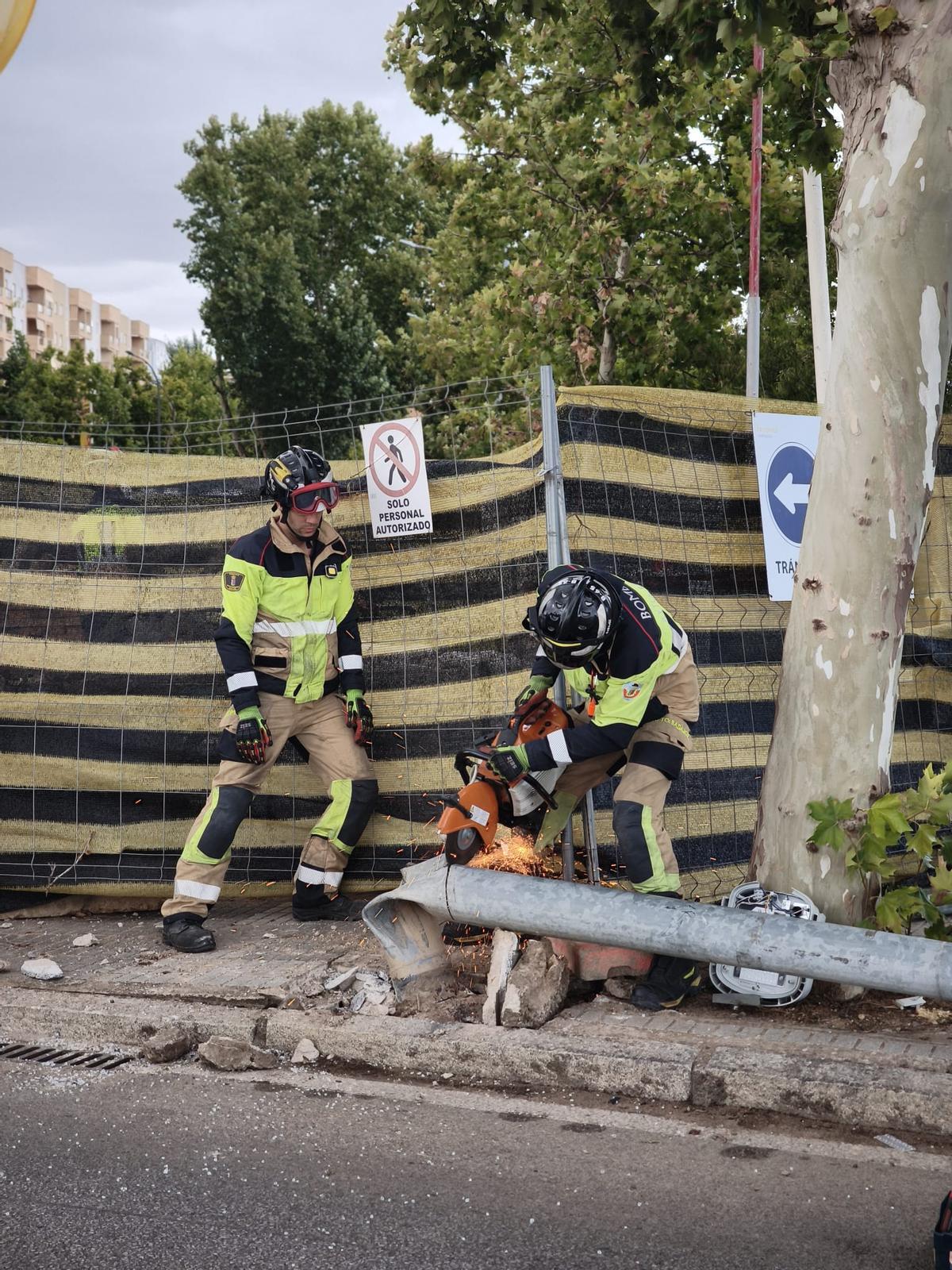Los bomberos cortan la farola derribada con una radial.