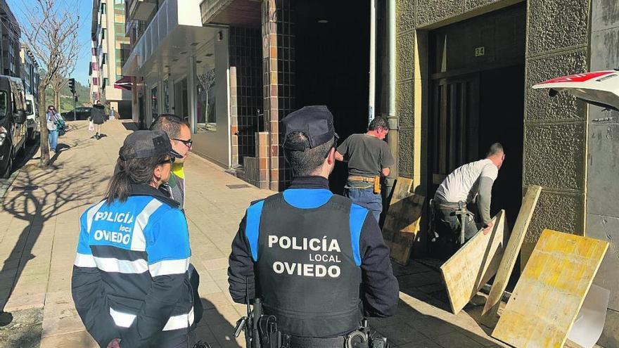 Los operarios tapiando la entrada al edificio de la calle Torrecerredo junto a una pareja de la Policía Local.