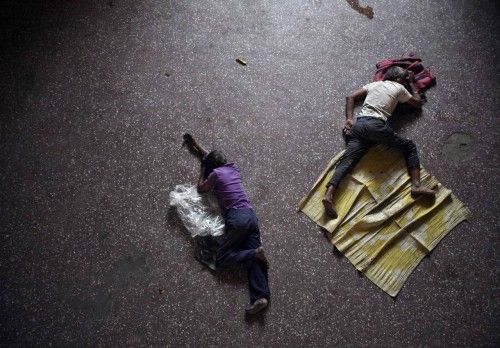 People take a nap on the floor of a bus station on a hot summer day in Jammu