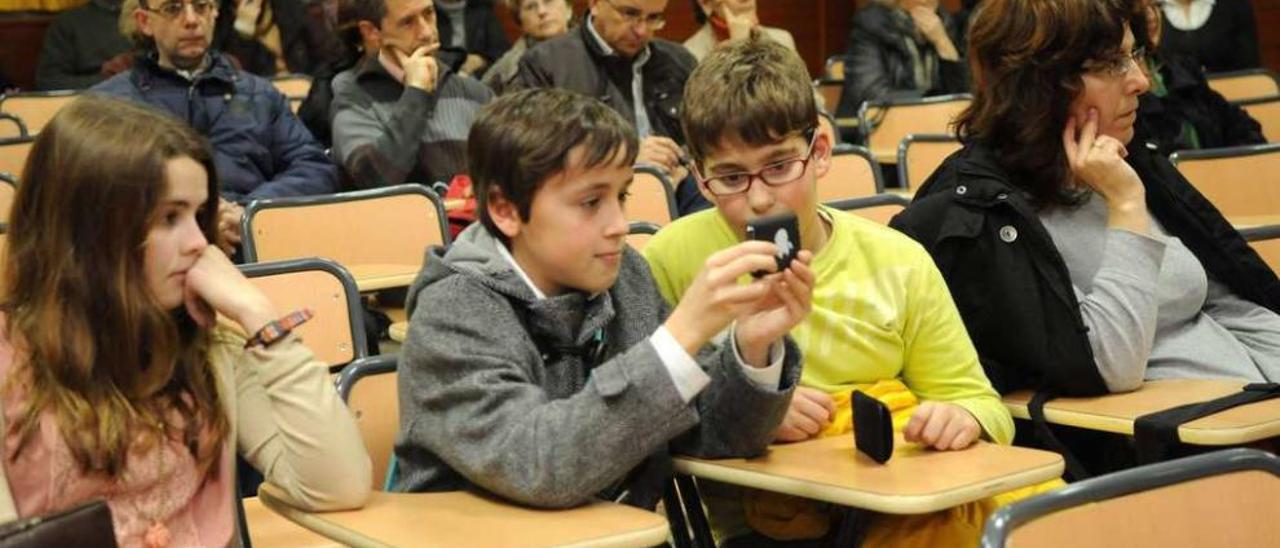 Dos adolescentes manejan un teléfono móvil durante una charla sobre adicción a internet en un instituto. // Gustavo Santos