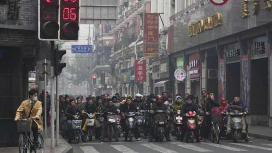 Usuarios de motocicletas y bicis esperan ante un semáforo en Shanghái.  // Reuters