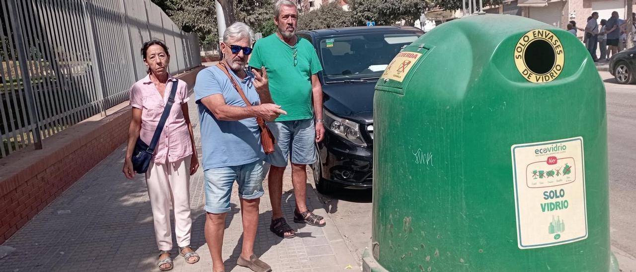 Julio Retamero con dos vecinos señala el único contenedor de reciclaje que sobrevive en su sitio, un año después del incendio.