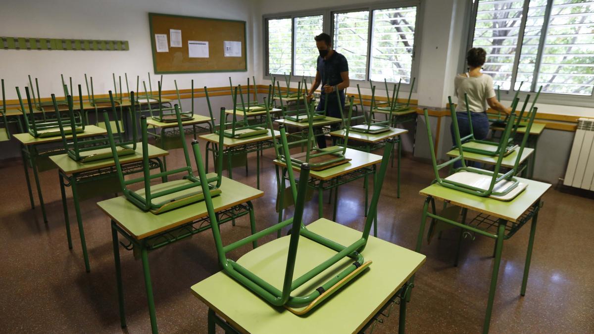 Dos profesores del instituto de La Azucarera, en Zaragoza, ordenan una clase del centro antes de cerrar su puerta definitivamente, este martes.