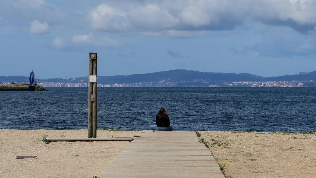 Una mujer observa el mar, sentada en una pasarela de playa de A Compostela, en Vilagarcía.
