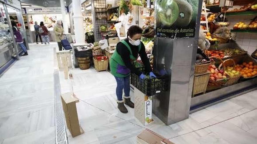 Celi Barro coloca una frontera de cajas para marcar la distancia de seguridad en su frutería del Mercado del Sur, en Gijón.