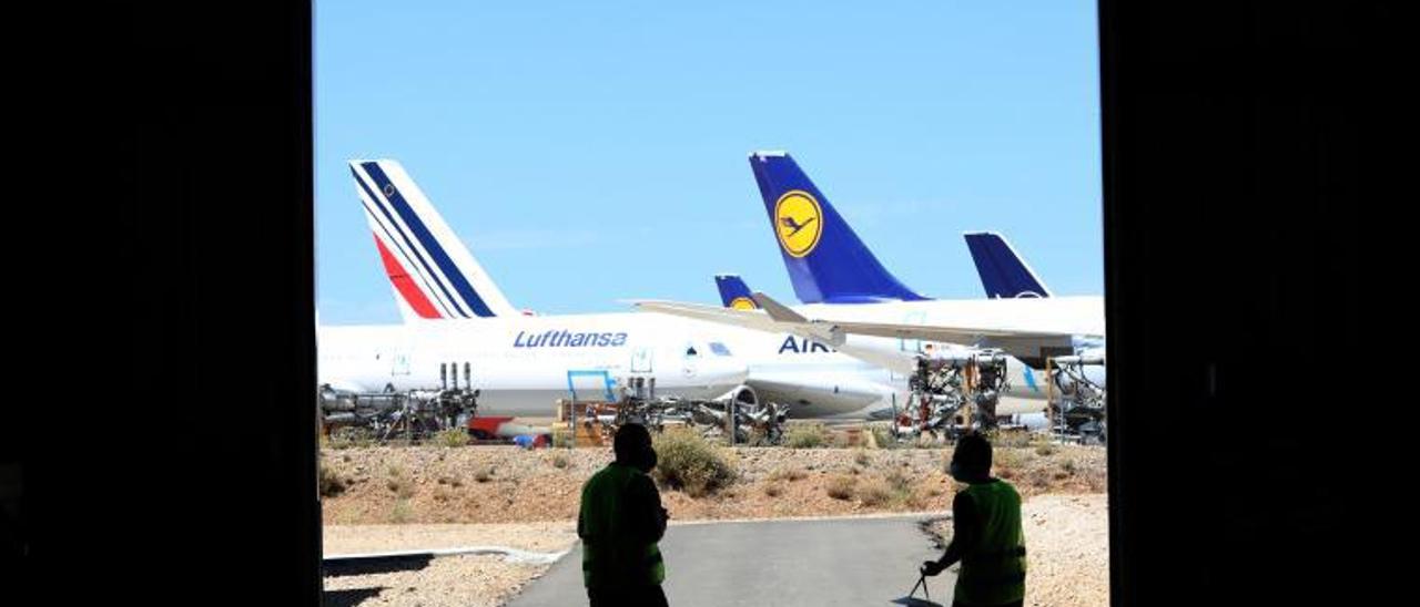 Dos operarios en uno de los hangares del aeropuerto de Teruel, con un avión la aerolínea Lufthansa al fondo. | ÁNGEL DE CASTRO