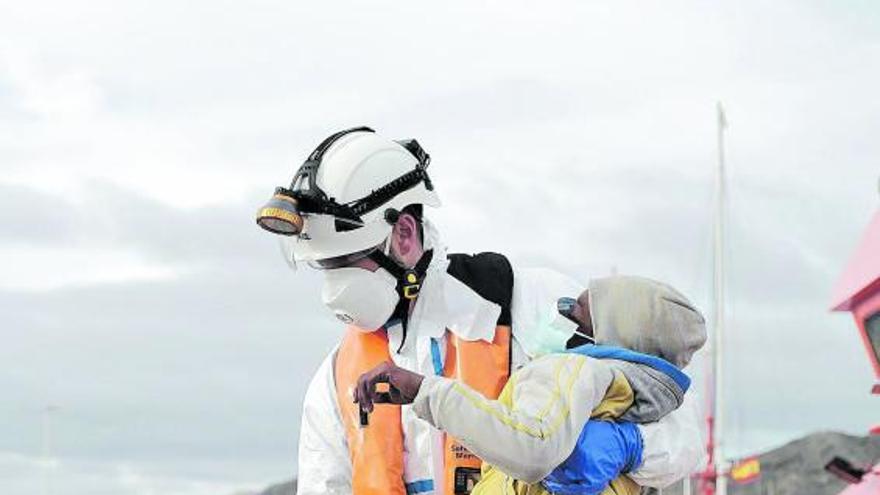 Un menor llegado en patera a las costas de Gran Canaria en brazos de un hombre protegido con un EPI.