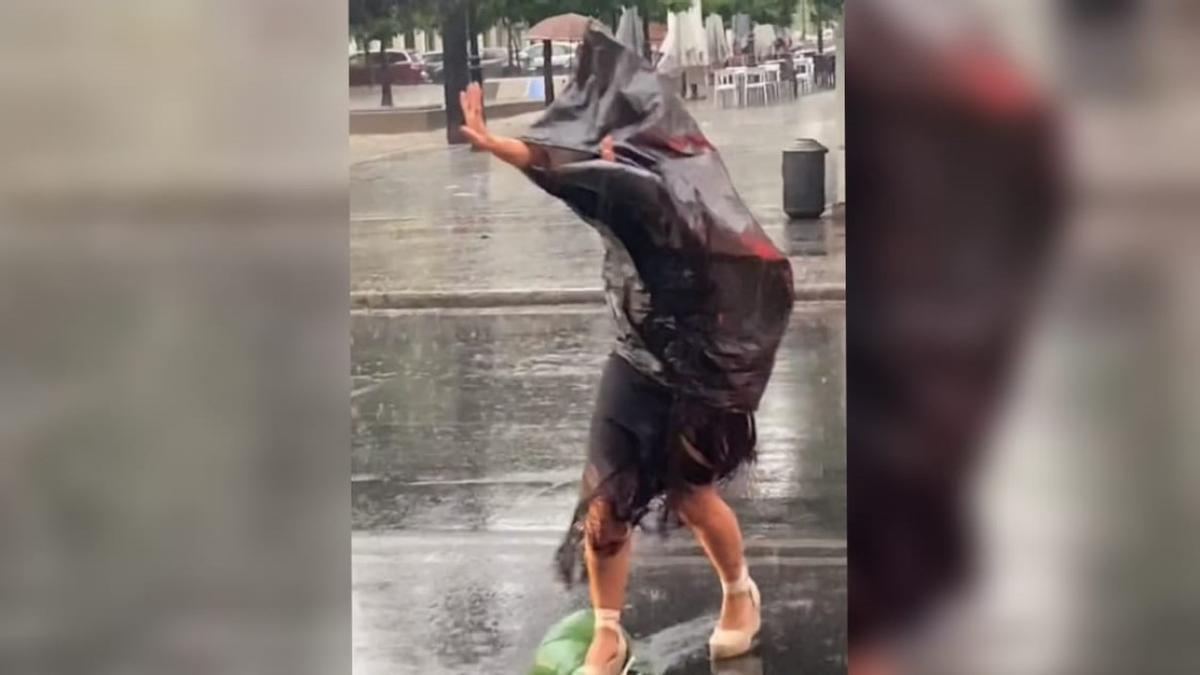 Una mujer cruza la avenida de las Ollerías bajo la lluvia protegiéndose de la lluvia con bolsas de plástico camino de la Feria de Córdoba,  en una imagen que se ha hecho viral.