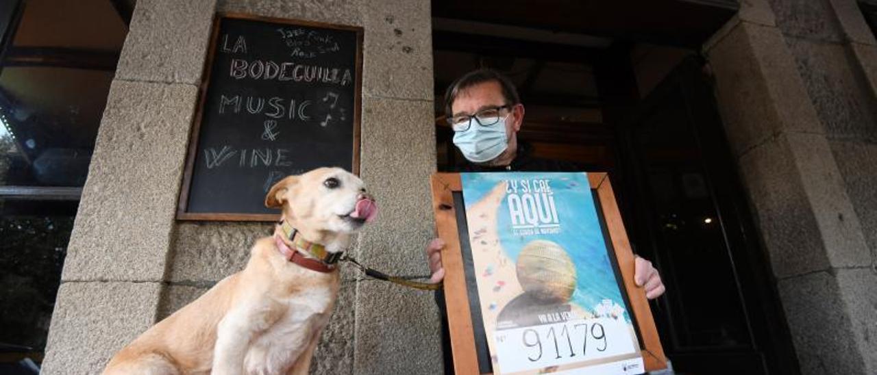 Claudio Massoni, en su bar, La Bodeguilla de Caldas, con su perro Remo y el cartel del premio.   | // G. SANTOS