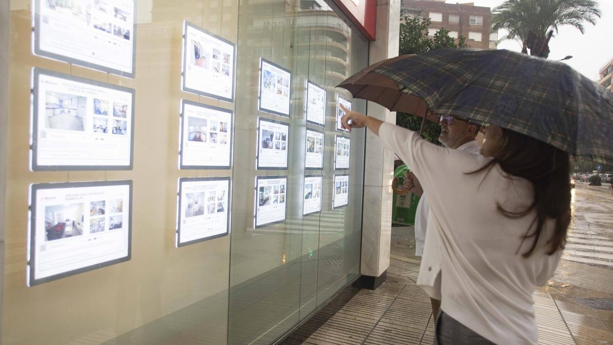 Dos personas observan algunas viviendas ofertadas en una inmobiliaria de Alzira, en imagen de archivo.
