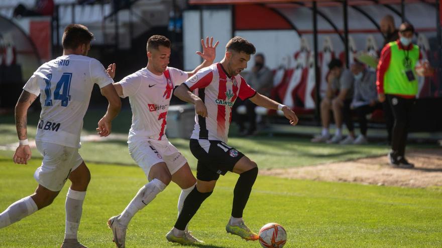 Carlos Ramos trata de zafarse de dos jugadores mientras Movilla analiza su pizarra en el banquillo. | E. F.