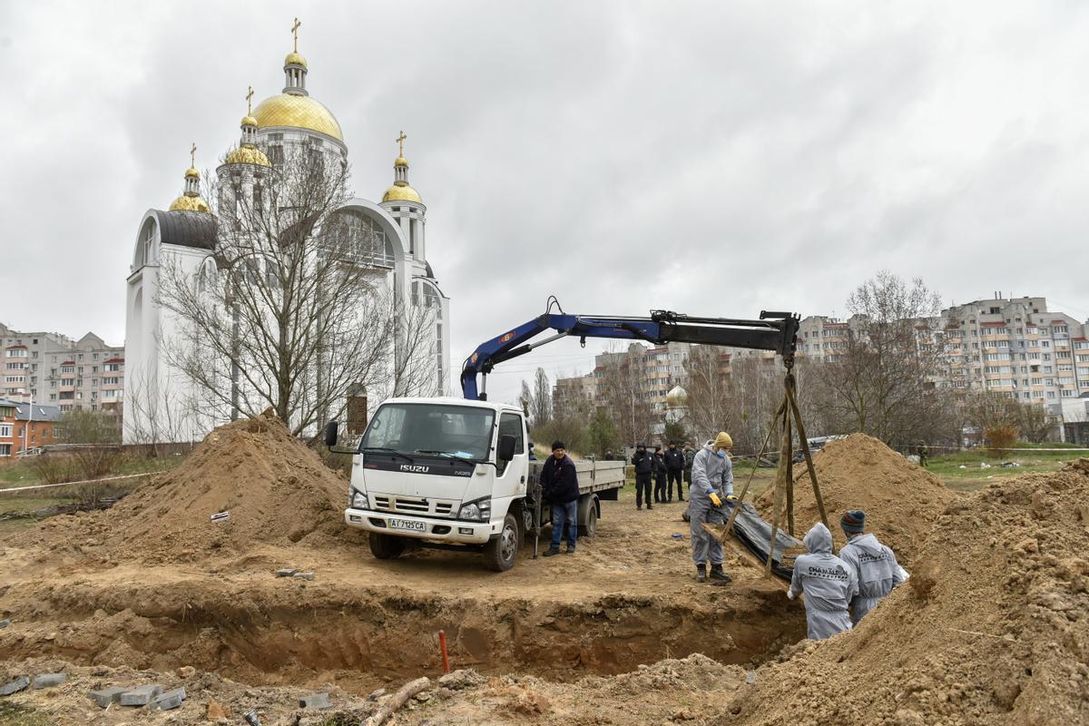 Trabajadores exhuman los cuerpos de la fosa común cerca de la Iglesia de San Andrés y Todos los Santos en la ciudad de Bucha en el área de Kiev (Kiev, Ucrania), el 13 de abril de 2022. Los investigadores forenses comenzaron a exhumar una fosa común en Bucha que contiene más de 410 cuerpos de civiles, según a los funcionarios ucranianos. El Consejo de Derechos Humanos de la ONU ha decidido iniciar una investigación sobre las violaciones cometidas tras la invasión a gran escala de Rusia a Ucrania