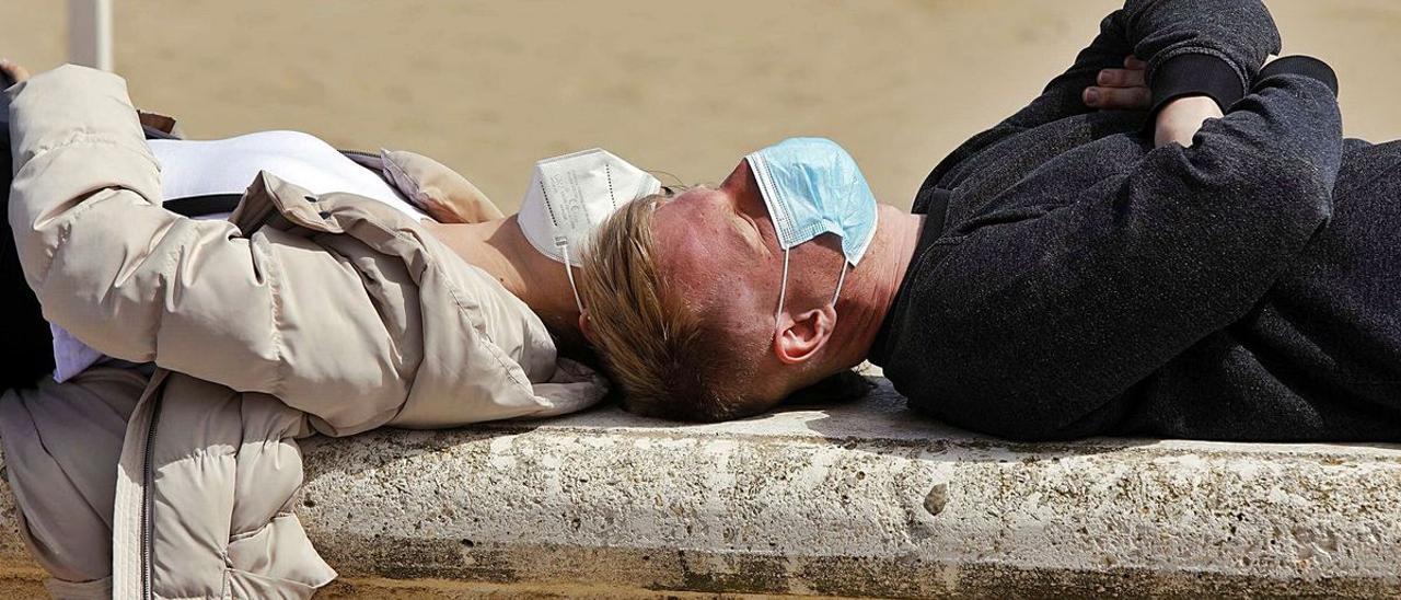 Una pareja toma el sol con mascarilla.