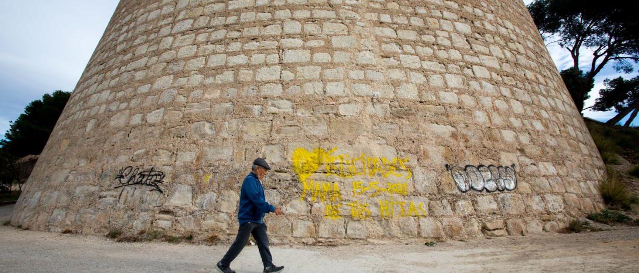 Un hombre pasa por delante del torreón grafiteado del castillo de San Fernando, el domingo. | JOSE NAVARRO