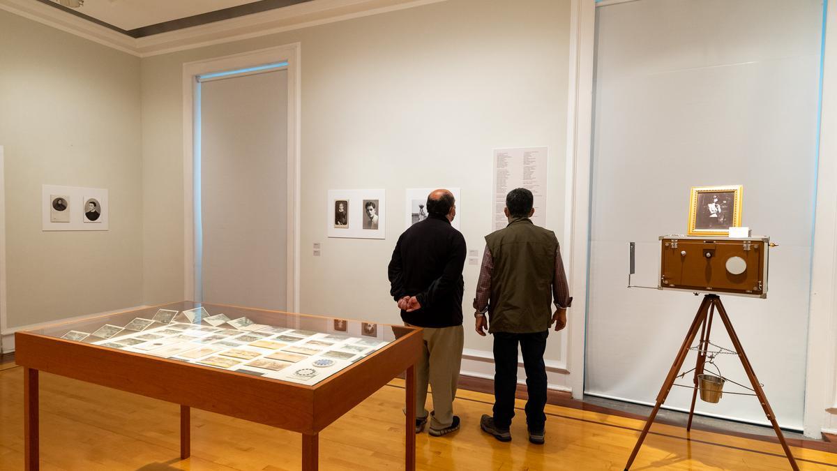 Dos visitantes leyendo el listado de los fotógrafos y agrupaciones de la isla en la sala Manolo Millares / Elvireta Escobio