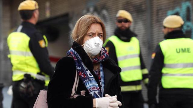 Una mujer camina con una mascarilla junto a miembros de la UME.
