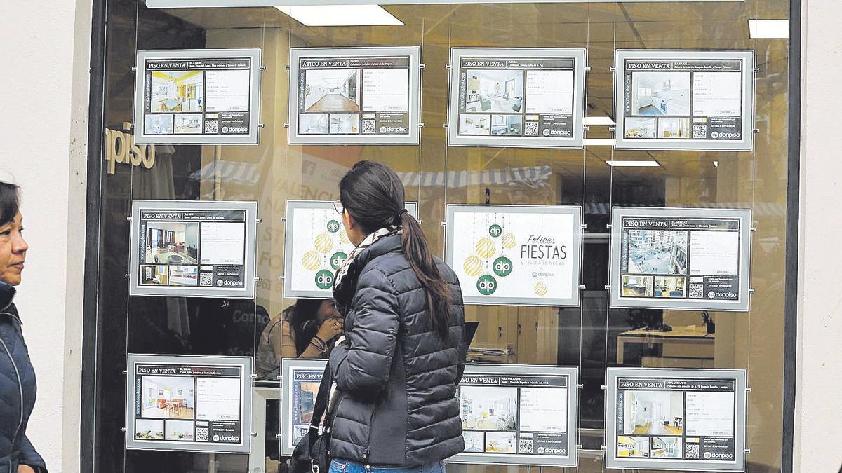 Una mujer mira las ofertas disponibles de viviendas en el escaparate de una inmobiliaria.