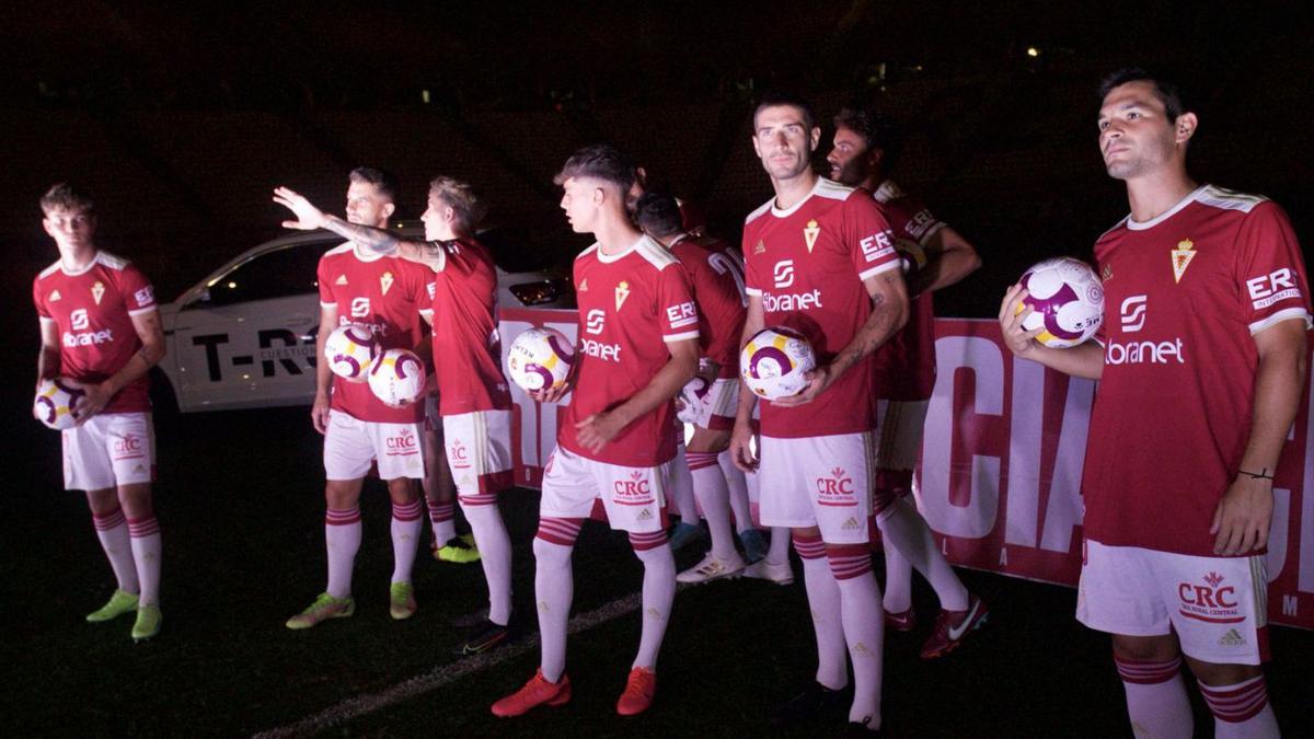 A la izquierda, los nuevos jugadores del Real Murcia se preparan para lanzar los balones a los aficionados, y a la derecha,Miku y Pedro León miran a la grada.