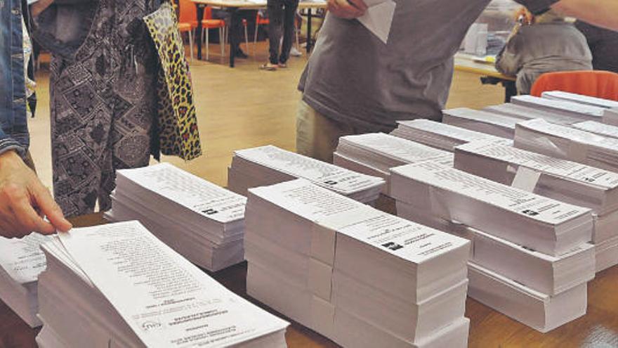 Votacions en unes eleccions municipals, amb les gruixudes piles de paperetes, tantes com candidatures, disposades en una taula del col·legi electoral