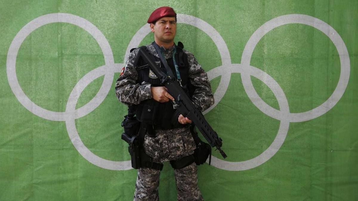 Un policía bien armado hace guardia delante de los aros olímpicos.