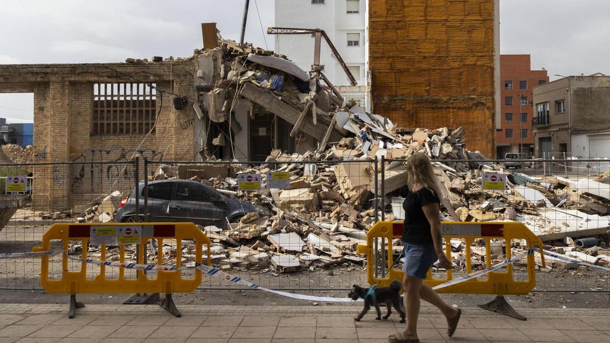 Una mujer paseando por la calle las Américas de Benetússer junto al edificio derrumbado.