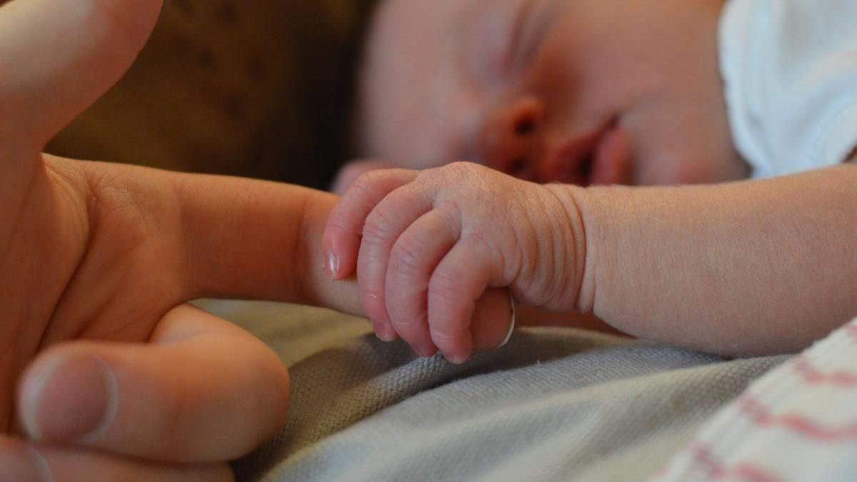 Un bebé recién nacido toma del dedo a su madre.