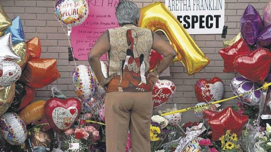 Una mujer frente a obsequios y flores en homenaje a Aretha Franklin.