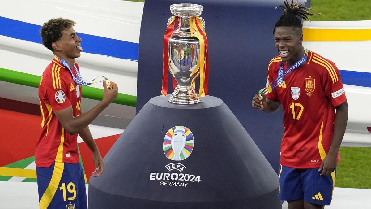 Lamine Yamal y Nico Williams festejan el triunfo con sus medallas delante del trofeo.