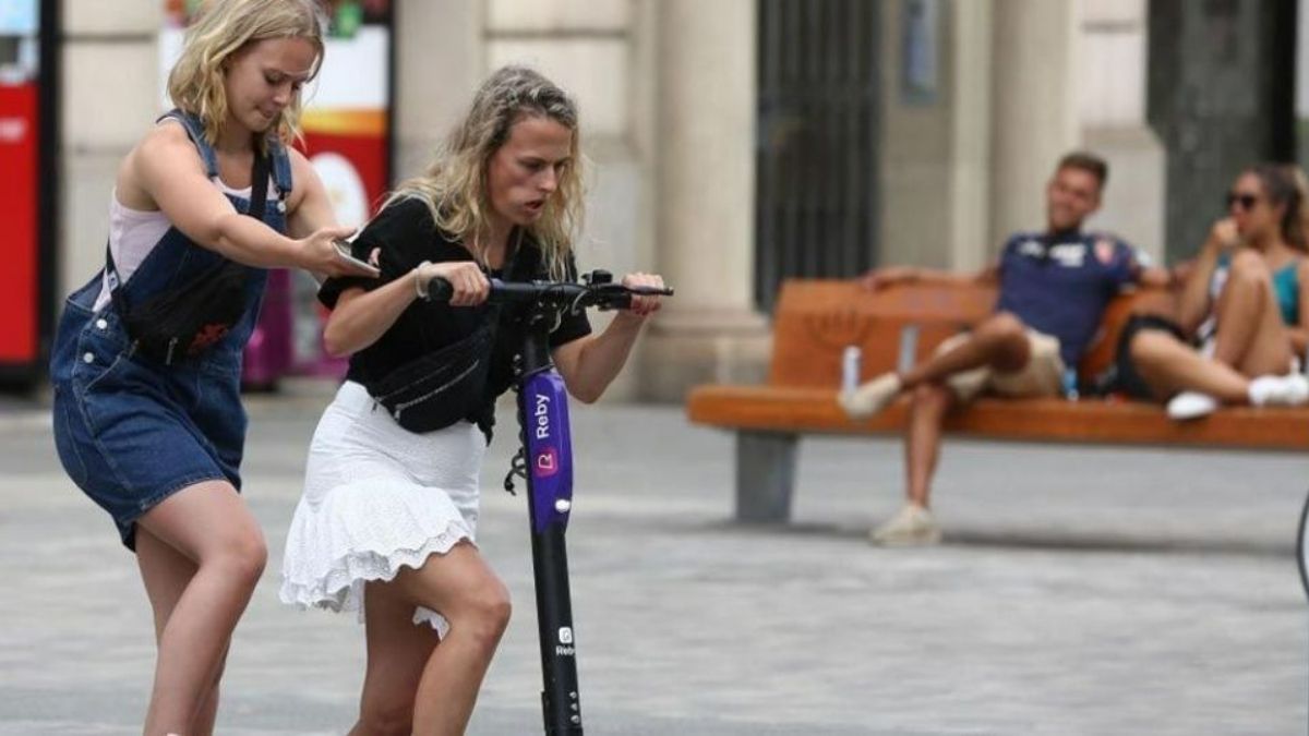 Dos jóvenes intentan subirse a un patinete compartido en Barcelona.