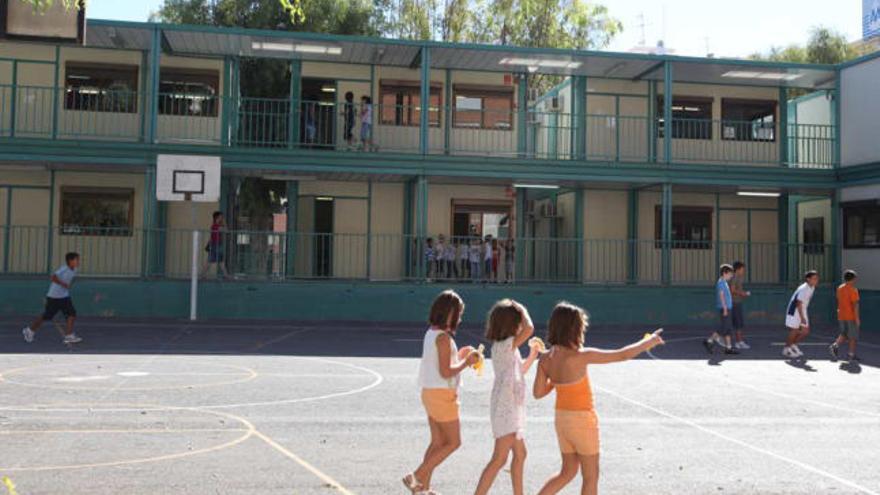 Varios niños juegan en el patio del colegio Benalúa de Alicante, con barracones al fondo.