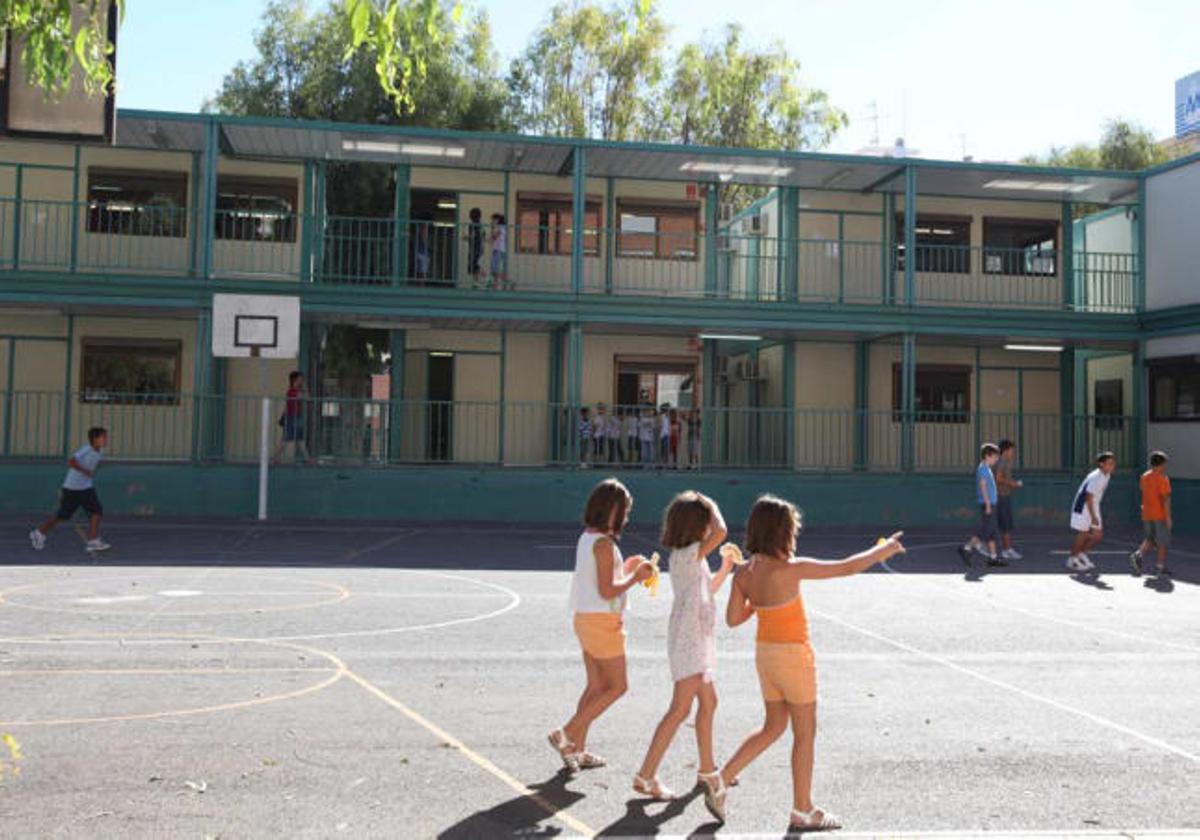 Varios niños juegan en el patio del colegio Benalúa de Alicante, con barracones al fondo.