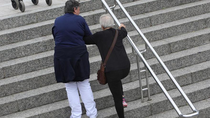 Una cuidadora ayuda a subir escaleras a una mujer dependiente en Santiago.