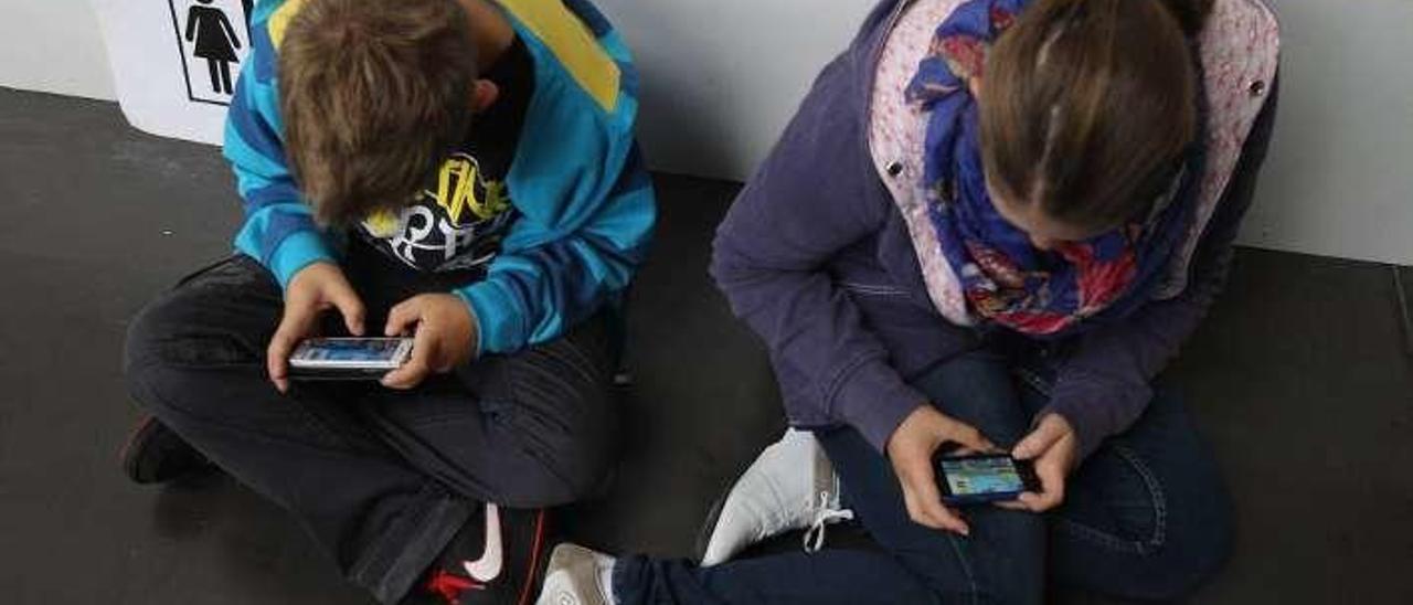 Dos niños usan sus teléfonos móviles.