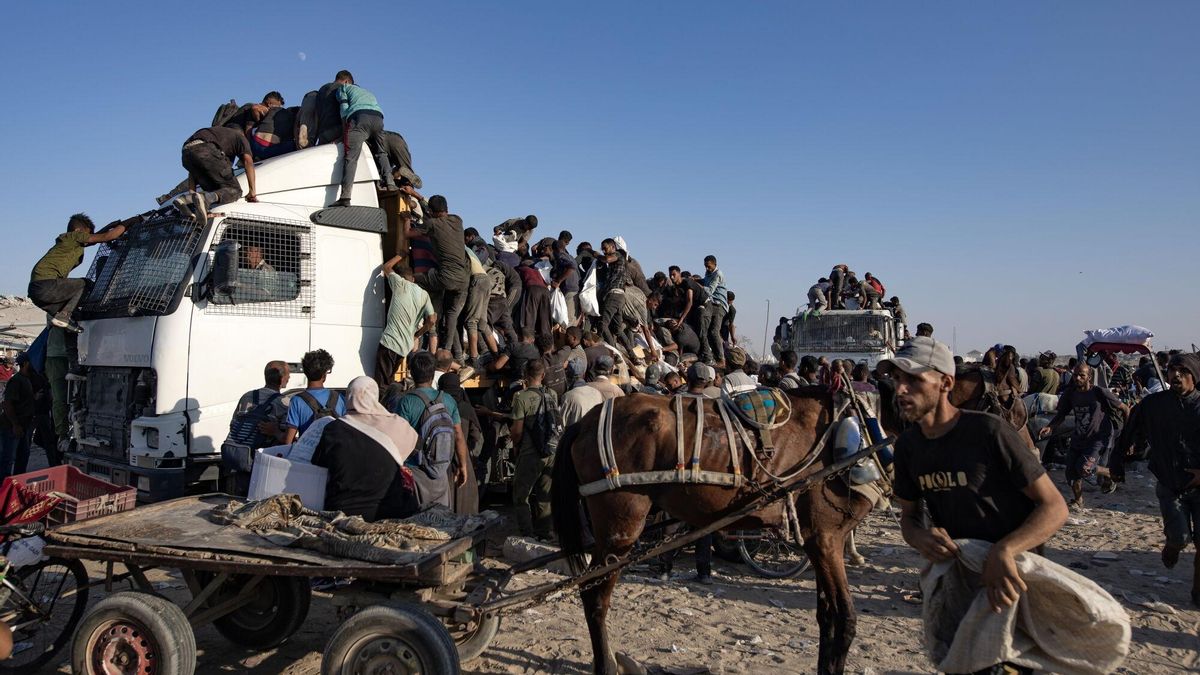 Palestinos desplazados internos suben a camiones de ayuda humanitaria para conseguir comida.