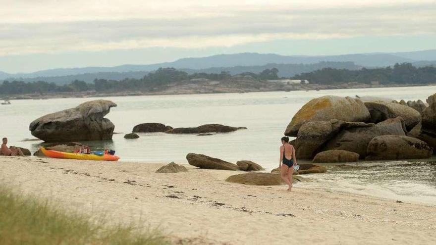 Una persona camina por las playas de Areoso con A Illa al fondo. // Noé Parga