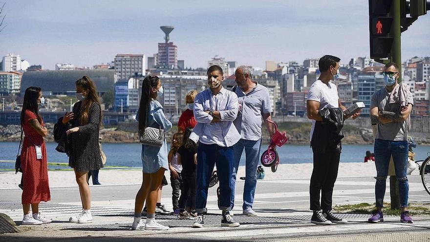 Varias personas con mascarilla esperan en un paso de peatones de A Coruña.