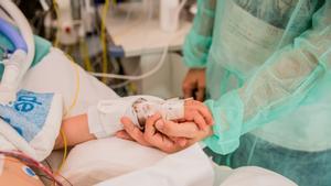 Un enfermero o enfermera da la mano a un paciente en una uci pediátrica de un hospital español