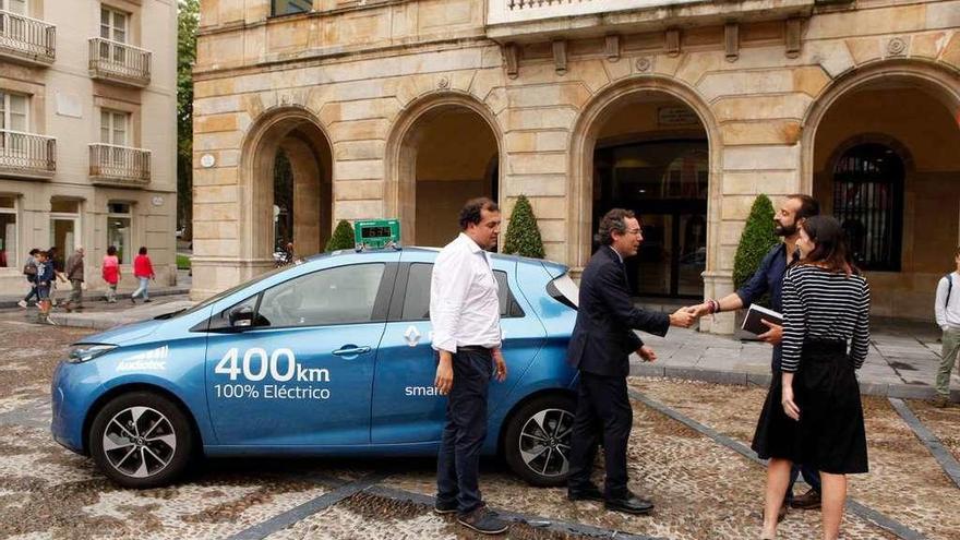 Los concejales Fernando Couto y Ana Braña saludan a Pablo Rodríguez y Eduardo Bustillo ante el coche eléctrico en el que se desplazan.